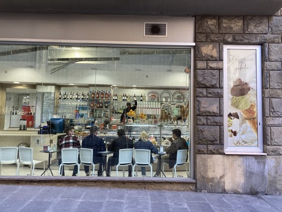 Photo of a ice cream cafe from the street showing people sat on chairs