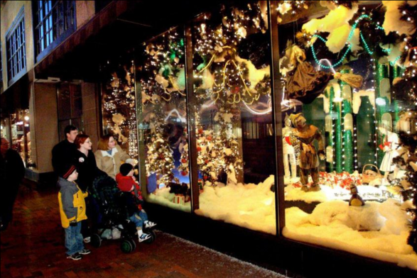 Color image of a family standing in front of a holiday store display window on Thanksgiving in Northeast Ohio. The photo shows a family of two parents and three children in cold-weather clothing and jackets, admiring a downtown store window recreation in the former O'Neil's Department Store.