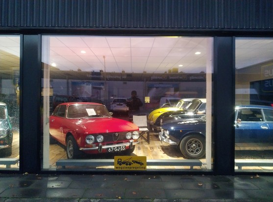 A red and a blue automobile in a illuminated shop window.