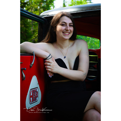 Woman in a strapless dress posing in the doorway of a vintage car.