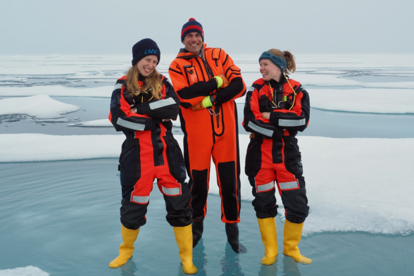 Three people standing in an Arctic melt pond, grinning and laughing.