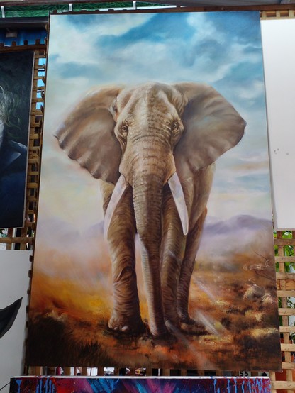 a painting of a large elephant, the painting is tall horizontally, the sky is blue with some clouds, the ground dry, some grasses sticking up