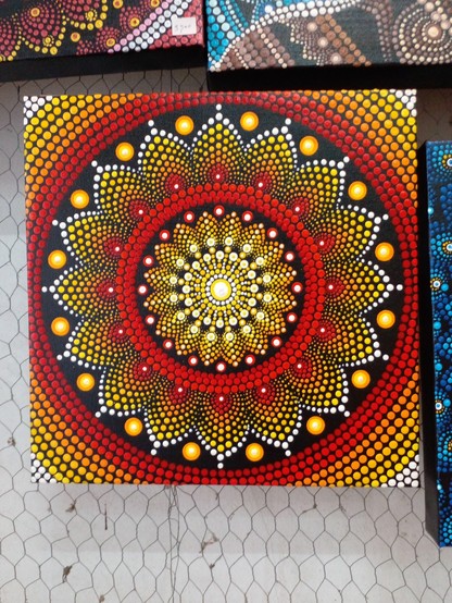a mandala painting, it is solar-themed, it is done with red, yellow, orange, and white on black