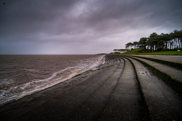 Shot along concrete steps forming sea front, with stormy sky above and rough seas on left frame.