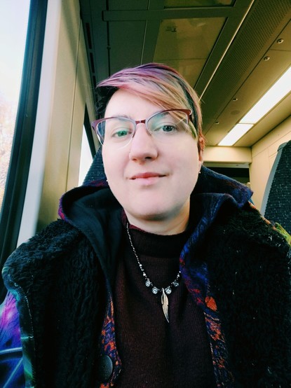 train selfie showing me with no makeup and wearing a big fluffy colourful coat