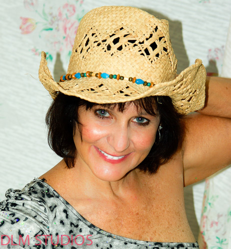 Head and shoulder shot of a Brunette cowgirl wearing a cowgirl hat. Big smile.