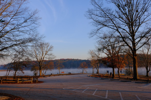 A lake view with the rising sun illuminating the lake, woods, and the parking lot