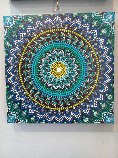 a mandala design done with green, yellow, white, and blue on black