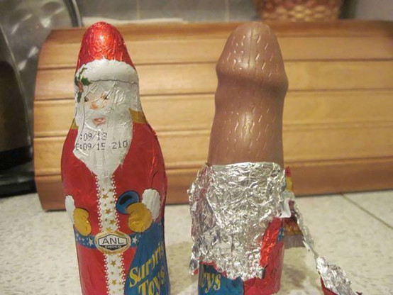 A photo of two hollow chocolate candy Santas wrapped in tinfoil that's made to look like Santa's coat, hat, beard, and face. Someone has peeled back the foil on one of the Santas to reveal a slender, round shaft that looks remarkably similar to a black dildo. 😲