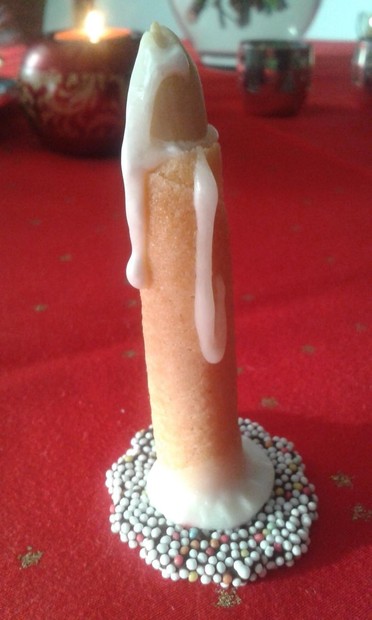 A photo of a tapered candle, tall and slender in its holder. On the outside, the candle is kind of... flesh colored, for some reason, and near the top, some of the inside wax, which is white, has oozed and dripped down the sides of the candle. The whole thing looks suspiciously like a penis dripping with semen. 😲
