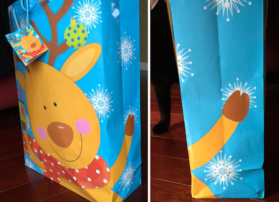 A photo (in two panels) of a holiday shopping/gift bag that has a cartoon reindeer printed on it. On the broad side of the bag, you can see the reindeer's smiling face and Christmas ornaments are hanging from its antlers. In the cartoon's background, large snowflakes are falling.
The reindeer is drawn with a big grin on its face and its front legs held widely in the air in celebration. The front legs are held so widely, in fact, that one of them extends past the broad side of the bag and wraps around it to one of its narrow sides. The second panel of the photo shows only the narrow side of the bag with the light brown-colored leg all by itself except for a few snowflakes, one of which appears to be "exploding" behind the hoof, which is dark brown. If you only look at the narrow side of the bag, it looks like it's printed with a brown, circumsized penis with a large head on it in mid-ejaculation (from the snowflake drawn behind it). 😲