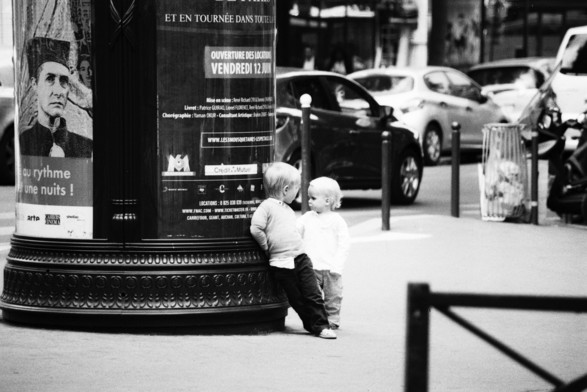 Deux enfants adossés a une colonne Morris, noir et blanc.