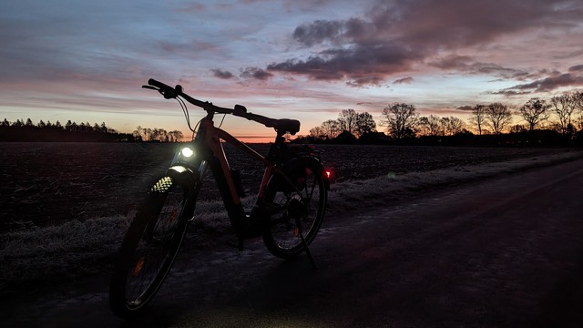Ein Mountain-Bike von vorn aufgenommen vor Sonnenaufgang. Der Himmel zeigt schon einen orangenen Streifen.