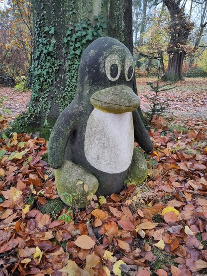 Ein Tux auf einer mit Herbstlaub bedeckten Wiese im Park des Linuxhotels.