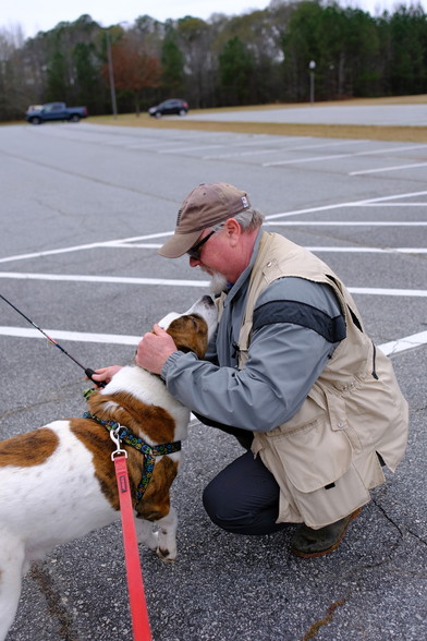 A man with a fishing rod crouching on a parking lot, making friends with a white and brown dog