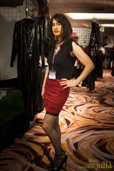 A crossdresser in a black top and red miniskirt stands on the domcon convention floor