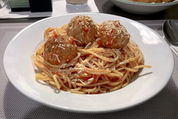 Three meatballs sit on top of a plate of spaghetti with tomato sauce, sprinkled with fresh parmesan cheese.