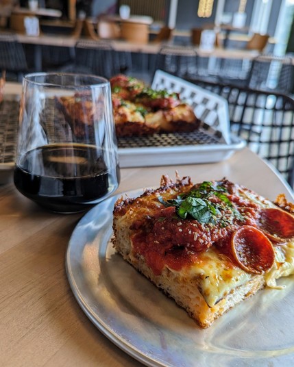 A slice of pizza and a black beer in a glass.