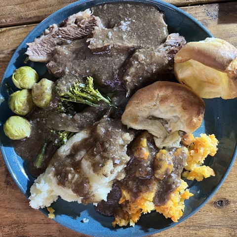 A plate of roast beef, Yorkshire puddings, mashed potato, mashed carrot and swede, sprouts and broccoli all covered with gravy.