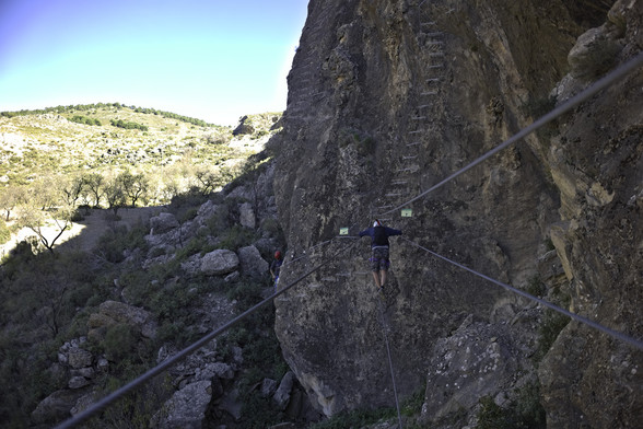 A person crosses a wire bridge across a gorge with some steps into the wall at the end