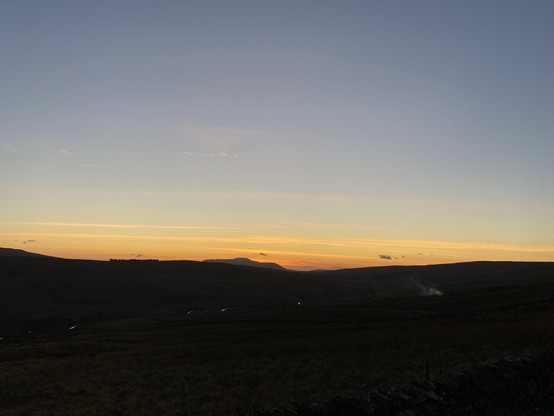 The sun has set, with blue sky fading to orange at the horizon, fields in the foreground are just about visible in the dimming light.
