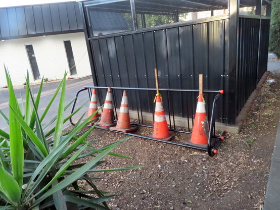 5 traffic cones put inside a bolted-together cheap wheelbender cycle rack. It's not very accessible nor very secure. It is currently in the dirt adjacent to a newly-built metal cage which is much much sturdier. The cage was built to lock up trash bins.