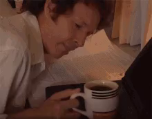 Ein Typ bückt sich erschöpft zu seinem Kaffeebecher auf einem Tisch. Er versucht zu trinken, knickt dabei dösend ab. Der Becher fällt um, der Kaffee ist verschüttet.