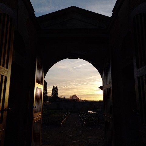 Grand stable gate style entrance to walled kitchen garden Tyntesfield at sunset. Silhouetted Sequoias can be seen in the distance