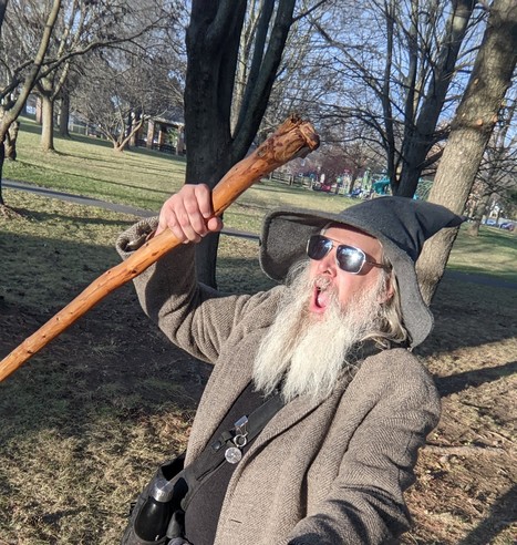 middle aged man with grey beard and gandalf style hat and staff yells into the cold air