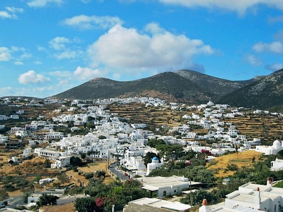 a photo of a town, all the buildings white, mountains in the background, blue sky with some fluffy clouds in it