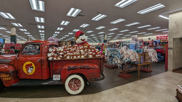A view inside the Buc-ee's gas station. You see a store area with clothing, and a red vintage truck with the Buc-ee's logo on it, and the back of the truck is filled up with plushies of the beaver mascot, with one of the plushies being an extra large plush.