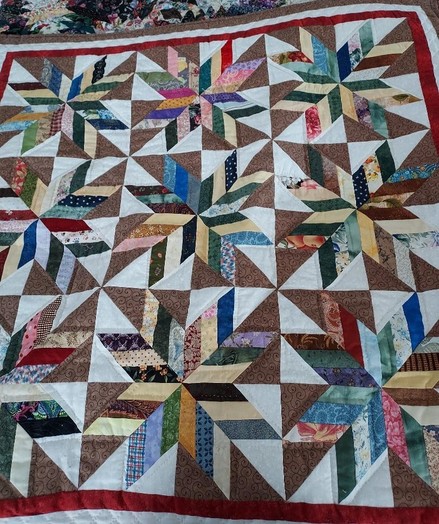 a quilt made up of many strips of triangular shapes making nine stars, a thin red border around it
