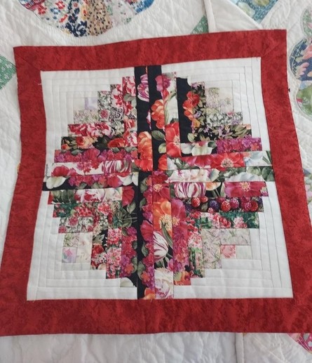 a quilt with a red border, white background inside it, floral pieces of red, pink, green, and black create a cross design inside a circle