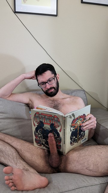 me sitting on my couch, one elbow on the back bent to lean my head against my hand, and the other hand holding a copy of the hardcover adventure book for The Wild Beyond The Witchlight campaign for D&D 5e. Helping prop up the half of the book that my hand isn't holding is my hard cock, pointing straight up so the book can rest against it. I'm sitting with my legs spread to show off my cock as much as possible, and i've got one foot posed to show off the sole to camera. My face looks perplexed with my brows furrowed, as though I'm unaware of my nudity because of concentrating on something in the book.
