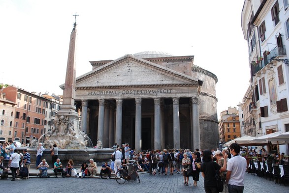 The famous landmark of the Pantheon, in Rome, Italy. People crowd the street and the fountain, in front.