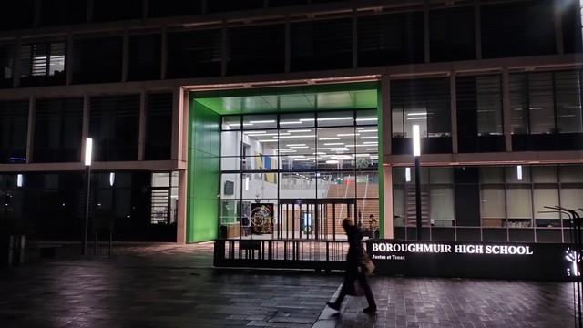 Boroughmuir High School at night, most windows dark, but the double storey height entrance brilliantly lit