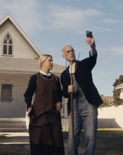 A couple dressed like the man and woman in the famous painting "American Gothic" recreating that photo as a camera selfie.