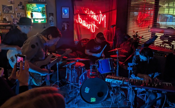 Emergency Group quartet in jamming formation with neon bar sign behind
