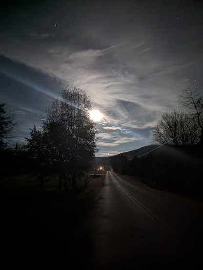 Night scene of a bright moon illuminating thin clouds and glinting off a rural road. A diagonal blue camera artifact bisects the sky.