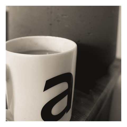 A mug with a Johnston ‘a’ on it. A hint of coffee can be seen with an out of focus clay pot in the background. The coffee is delicious.