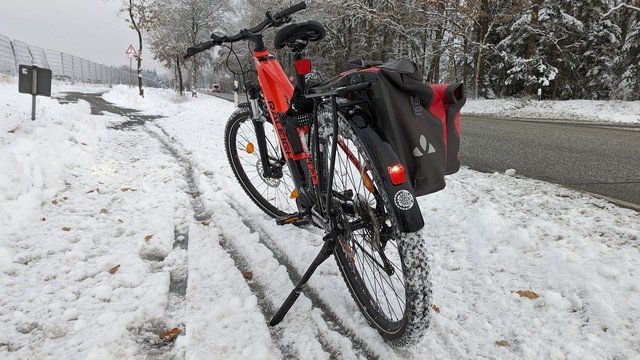 Ein rotes Raleigh Dundee Mountain Bike steht auf einem vereisten Fahrradweg an einer Bundesstraße. 
Am hinteren Schutzblech ist der Aufkleber "Frostpendeln 2023" zu erkennen.