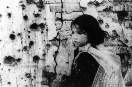 The titular girl passing a bullet-strewn wall.