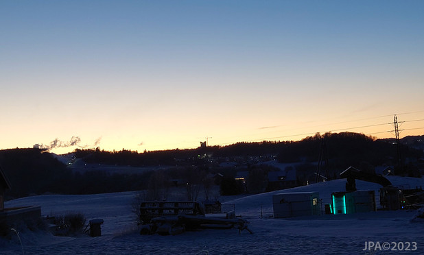 Kveldsbilde tatt fra Bratsbergveien viser TilleromrÃ¥det med det nye hotellet de bygger det nÃ¥, i siluett mot den orange solnedgangen.