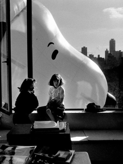 Head of Snoopy float from Macy's Thanksgiving Day Parade in New York City as viewed through a window (with people and a landline telephone by the window).