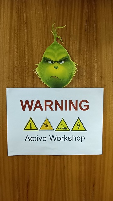 Door with a cut out of The Grinch's head above a sign reading "warning, active workshop"