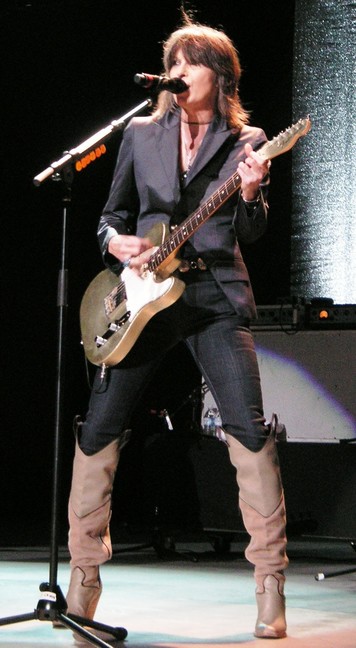 Chrissie Hynde tocando la guitarra sobre el escenario, con un traje de chaqueta negro y botas altas marrones. Jslonaker • CC BY-SA 3.0