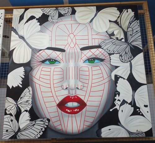a painting of an ivory-skinned woman's face, looking directly at the viewer, with red minimalist lines painted on her face, red lips, dark hair, a halo of butterflies around her face, she has green eyes