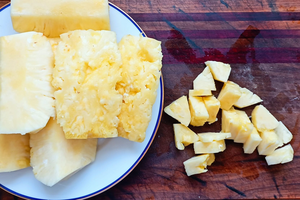 Auf einem Teller die von Schale und Strunk befreite Ananas, daneben auf dem Brett in StÃ¼cke geschnittene Ananas.