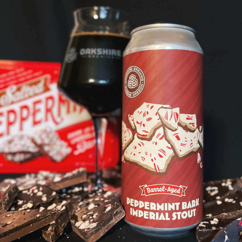 Can and a snifter glass of Barrel-Aged Peppermint Bark Imperial Stout from Oakshire Brewing of Eugene, Oregon (via their Facebook page). It's surrounded by peppermint bark candy with the candy box in the background.