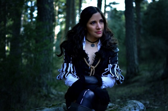 Laura cosplayed as Yennefer. She a is black-haired girl with a black jacket with puffy white sleeves and black leggings. She is sitting on a rock.